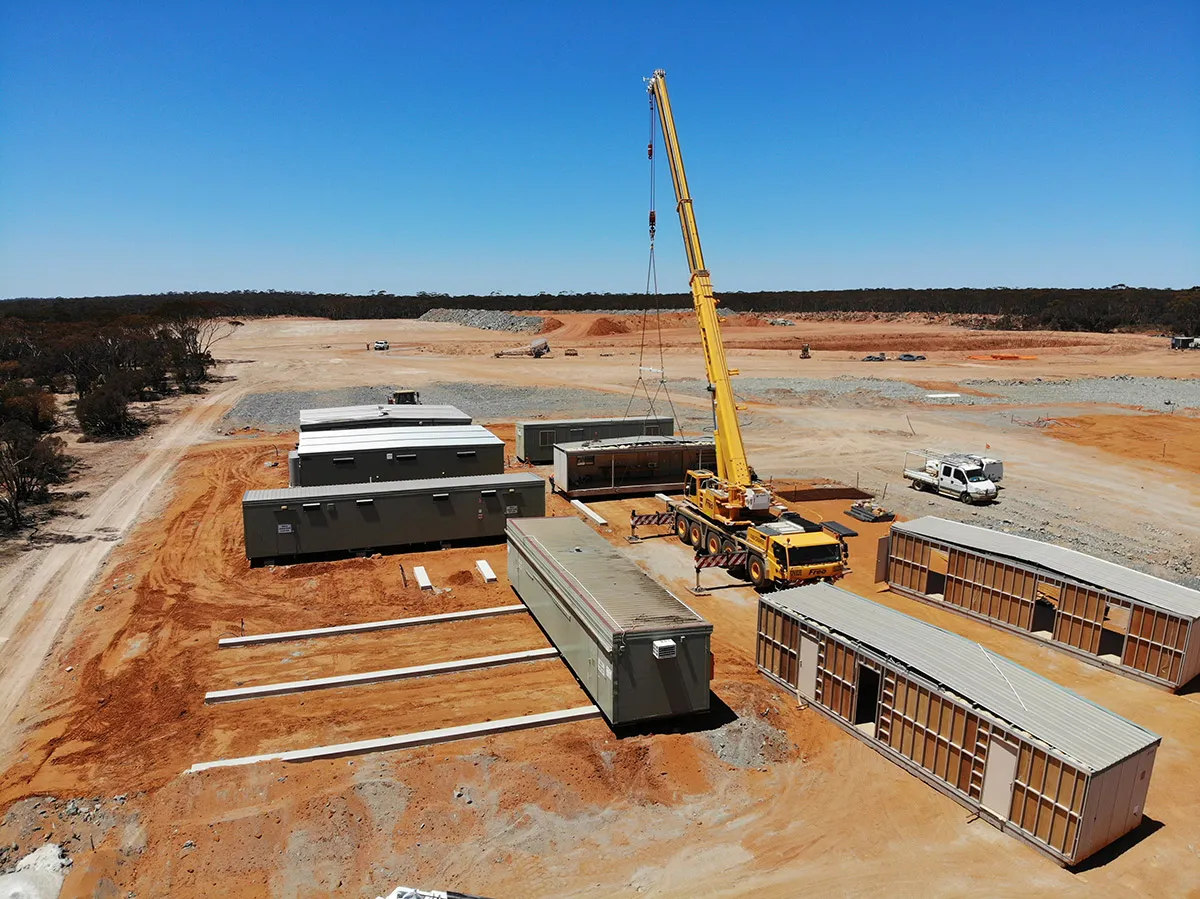 Aerial view of a mobile crane placing modular site buildings on concrete footings at a newly cleared mine site