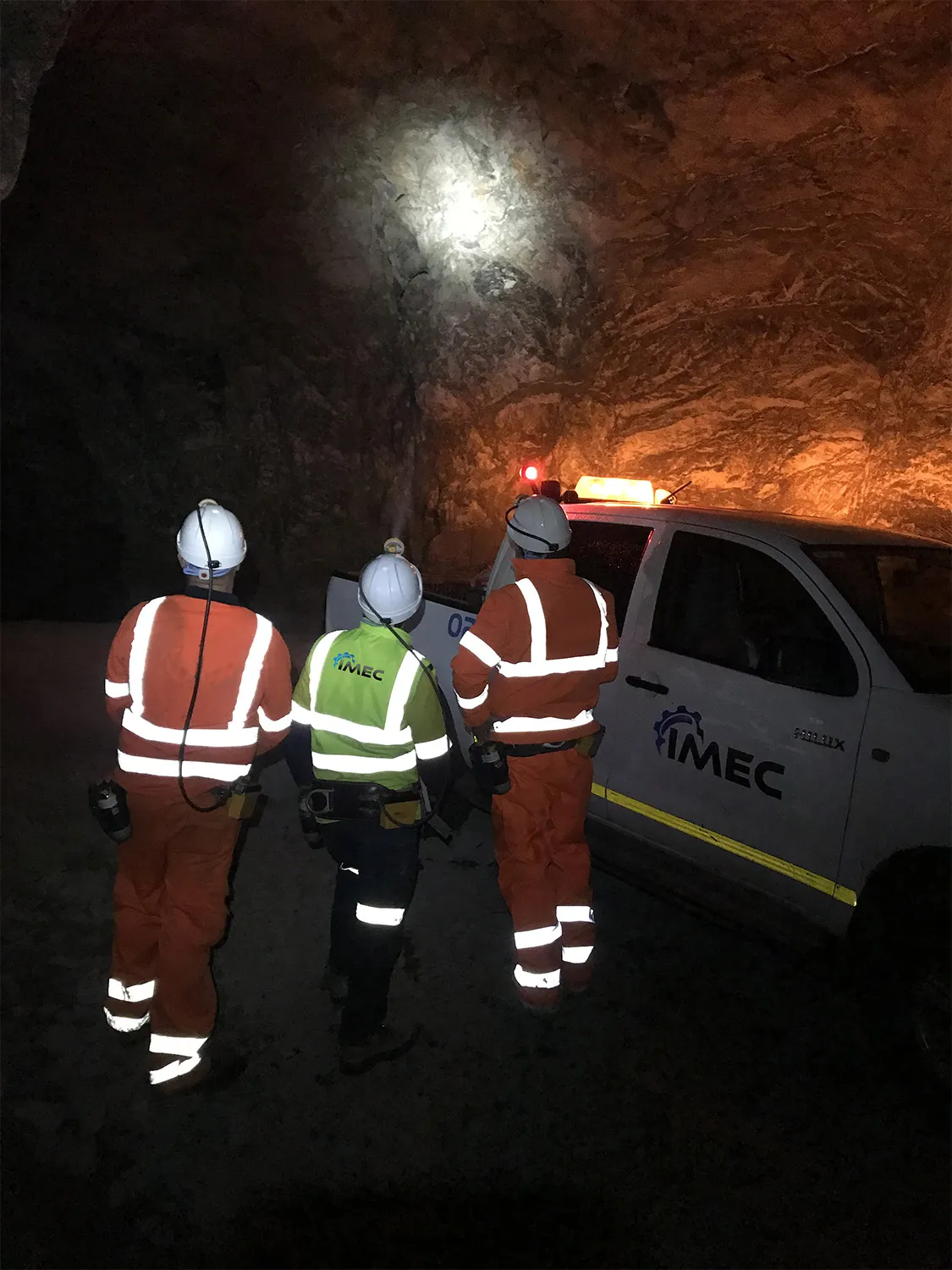 Three IMEC engineers in hi-vis and hard hats beside a vehicle underground at a mine site