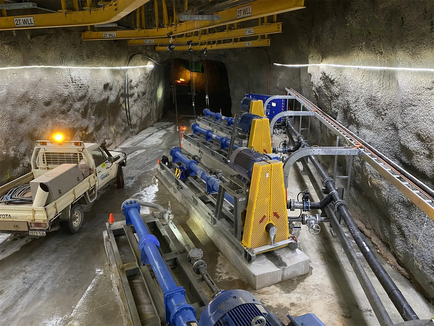 Underground mine dewatering pump station with motors and piping beside a utility vehicle in a tunnel
